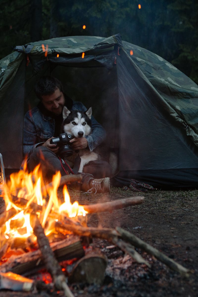 Cozy camping scene with a man and his dog by a campfire at night.